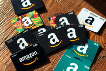 A collection of physical and digital Amazon gift cards displayed on a wooden surface, showcasing various designs and denominations